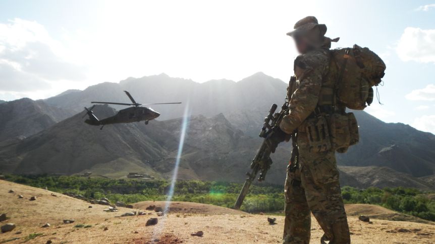 SAS soldier overlooks valley in Afghanistan as Black Hawk helicopter flies past in 2012.